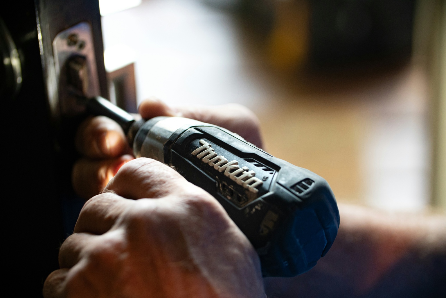 Hands using a Makita drill to adjust a door lock